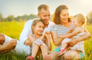 Young family sitting on the ground outside on a sunny, warm day.