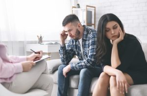 A young, upset couple sitting next to each other on a couch.