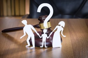 White silhouette of two parents hold ing a child's hand in front of a gavel.