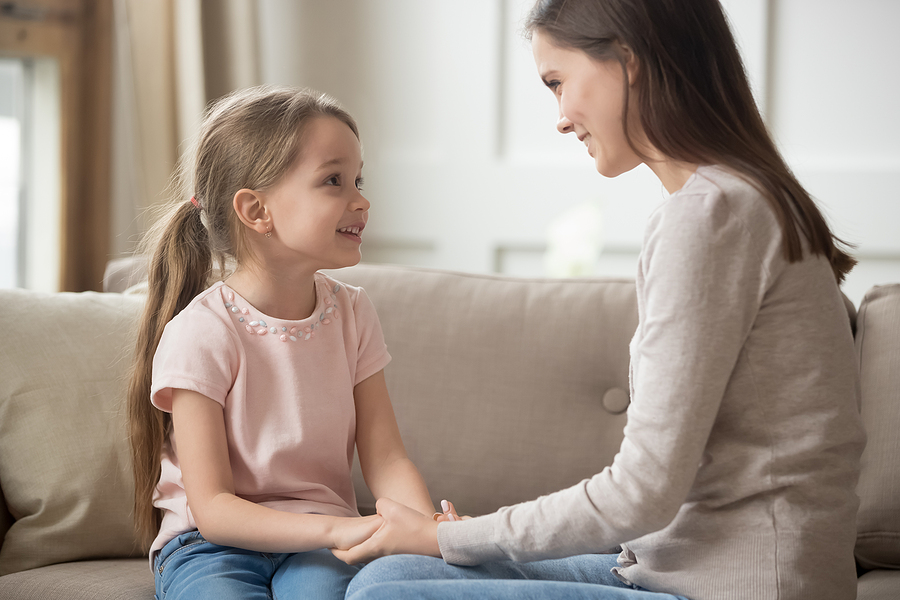 Loving mother and child holding hands talking sitting on sofa