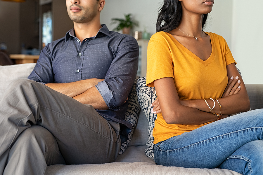 Divorcing couple sitting back to back on a couch with their arms crossed.