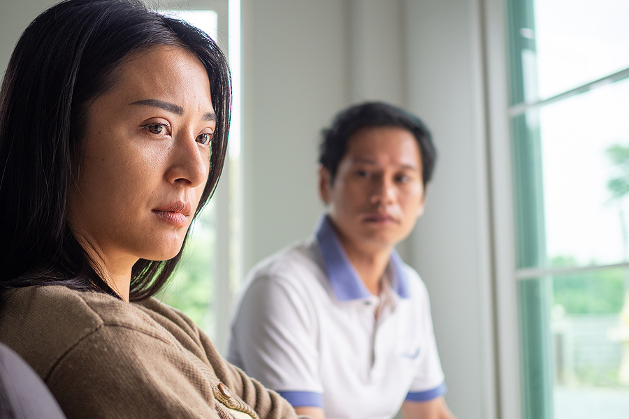 Divorced sad couple sitting in the same room. The wife is looking away from the husband.