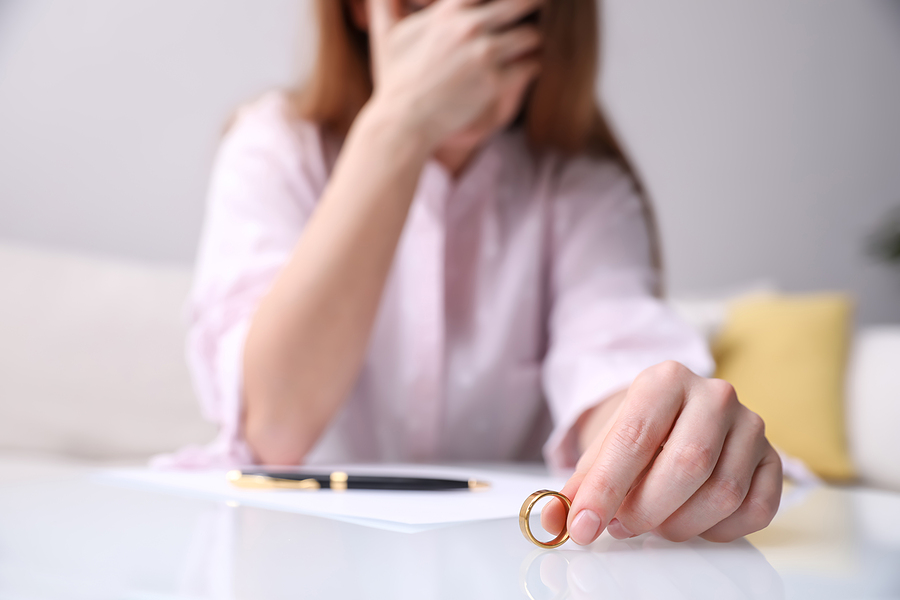 Woman with her head in her hands holding her wedding ring in her other hand.