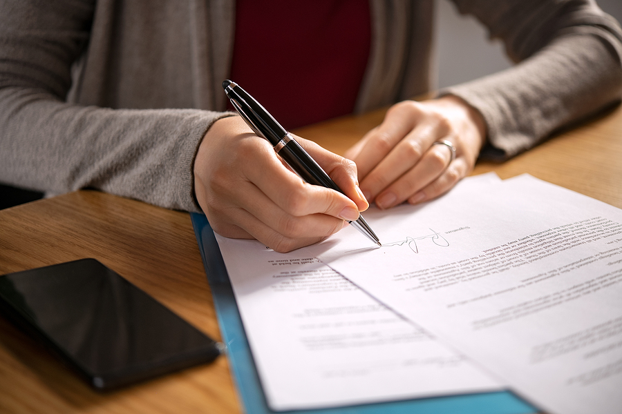 Close up of woman signing papers at a desk.