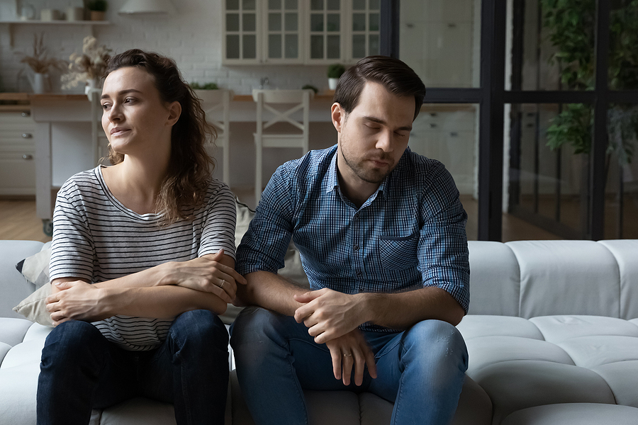 Depressed unhappy young couple sitting on sofa deciding how to sell the house after a divorce.