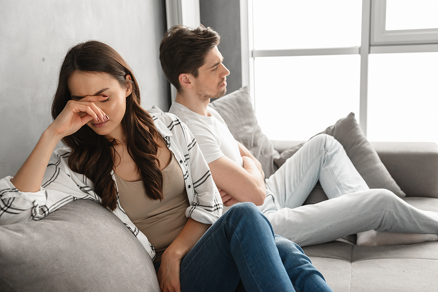 Photo of disappointed couple sitting together on sofa at home with upset look and expressing quarrel isolated over white background.