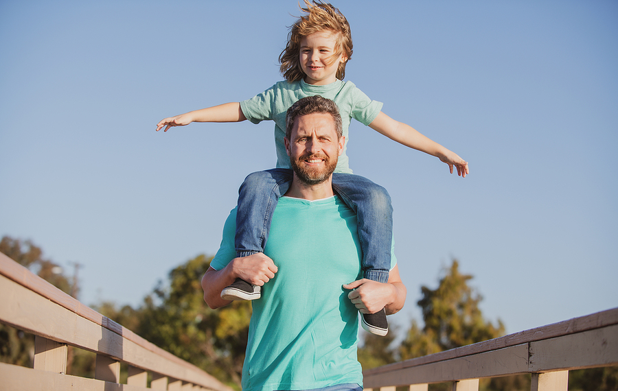 Single father with child on his shoulders walking at a park.