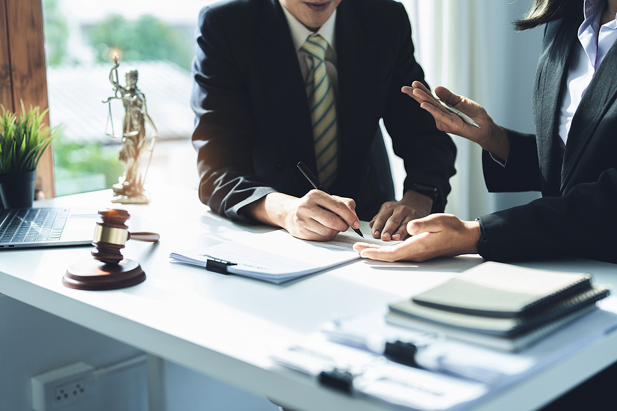 Two people in suits signing a paper with gavel on the desk in front of them