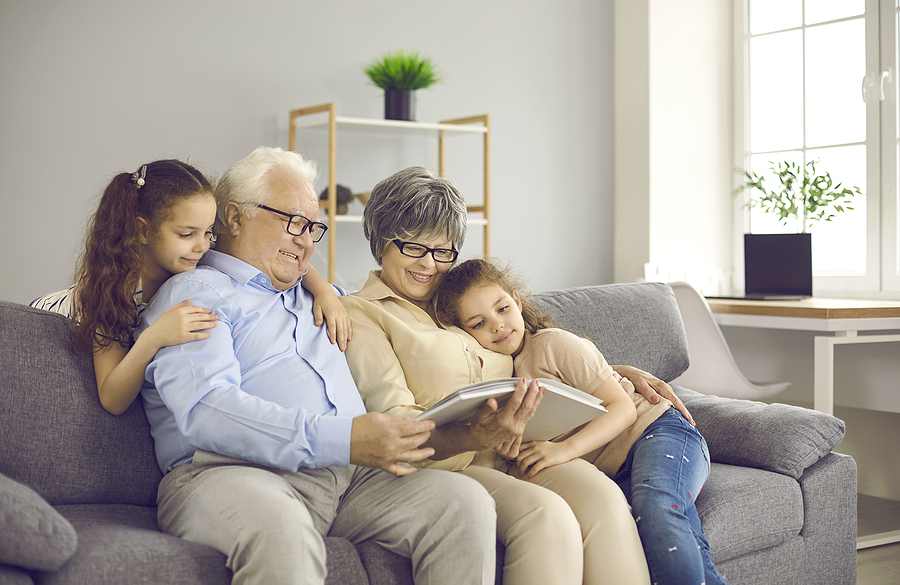 Happy grandparents with two grandchildren browse family photo album and share happy memories.