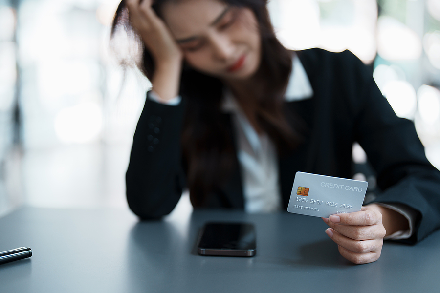photo of a young woman sitting at a table holding a credit card looking stressed