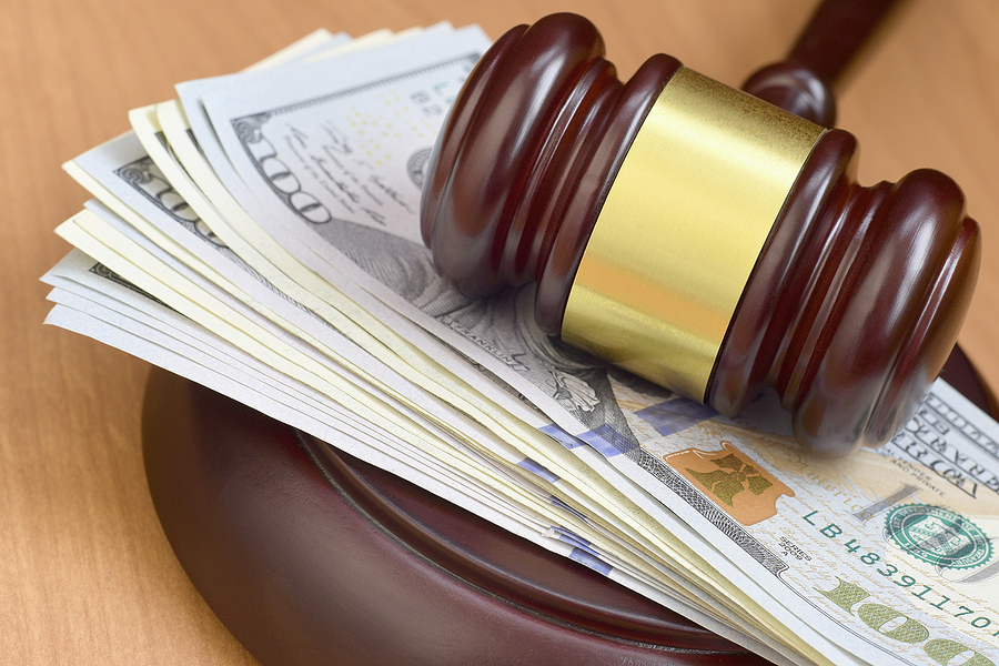 judge's gavel sitting on a pile of money on a wooden table