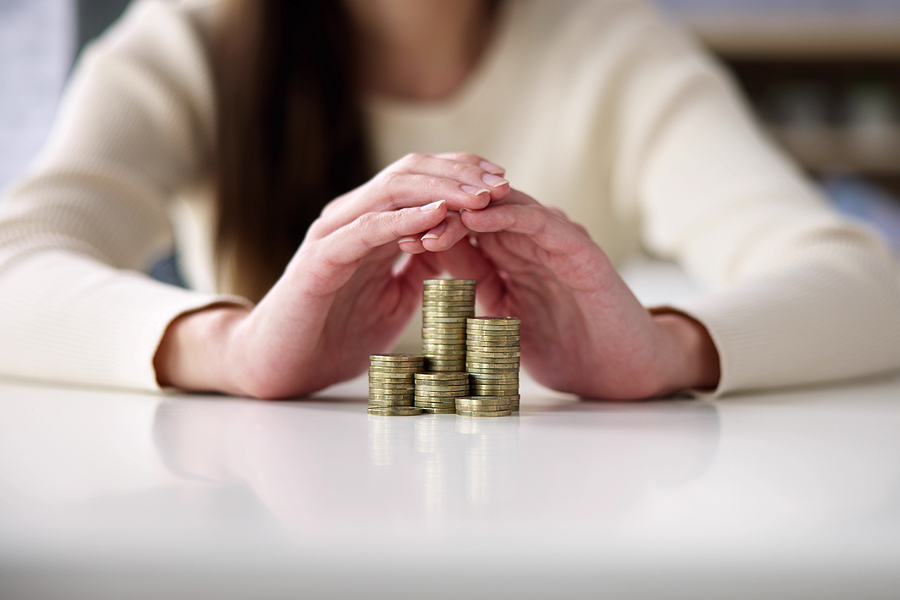 woman holding her hands over a pile of coins symbolizing protection of finances
