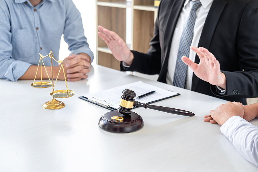 Couple sitting across from each other at a lawyers desk while lawyer resolves conflict