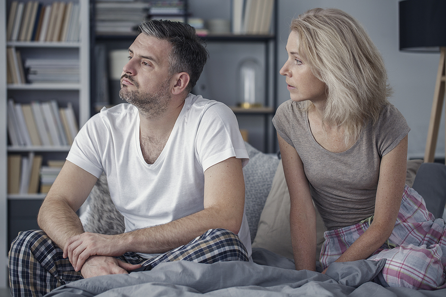 Middle-aged married couple sitting on a bed, having problems with communication