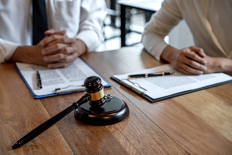 Close up of husband and wife sitting at a table with arms folded with a judge's gavel and legal paperwork between them. 