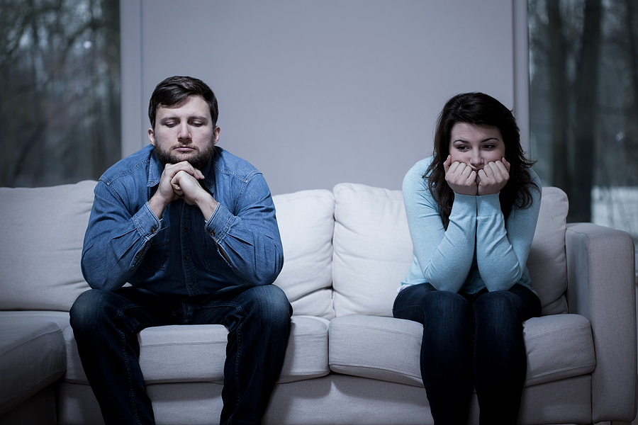 Couple sitting on opposite ends of the couch looking unhappy. 