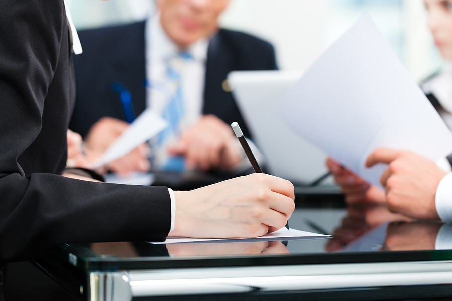 Business meeting at an attorney's office with a man in a suit in the background and a woman's hand writing notes. 
