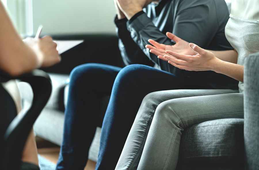 Closeup of a man and a woman sitting on a couch arguing in front of an attorney.