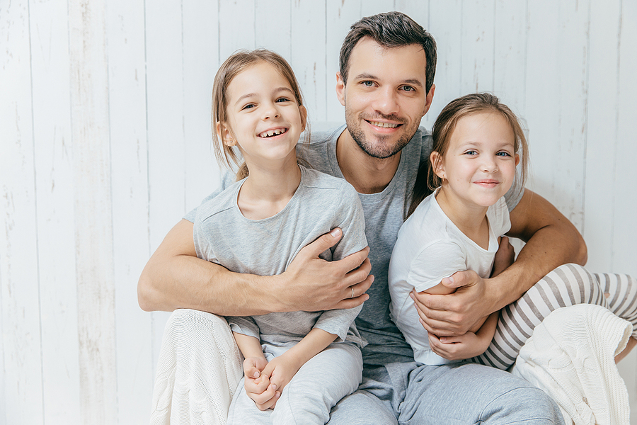 Father posing with his two daughters against a white background. 