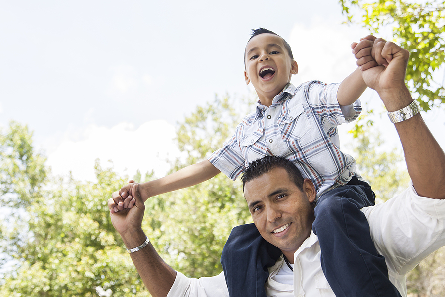 Father with son sitting on his shoulders outside.