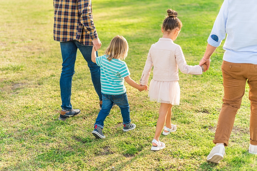 Two children holding hands and walking in the park with their dads.