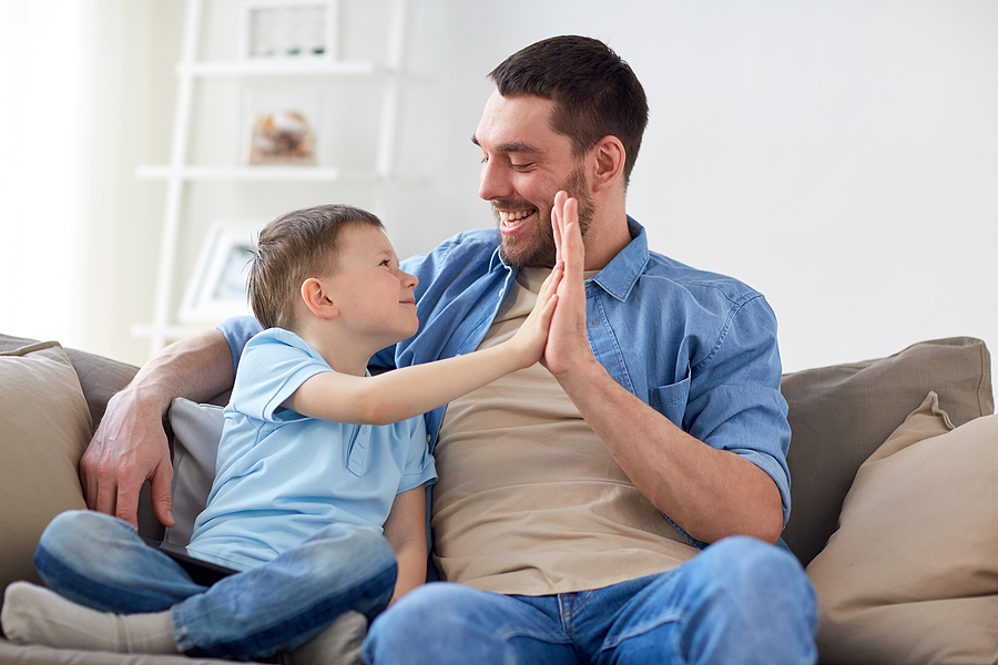 Single father giving his young son a high five on the couch